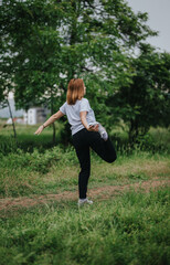 A woman performing a yoga pose on a grass trail surrounded by green trees. Emphasizes nature, relaxation, and healthy lifestyle.