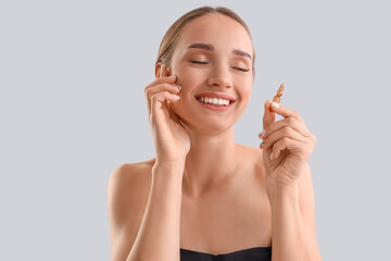 Happy young woman with ampoule on light background, closeup