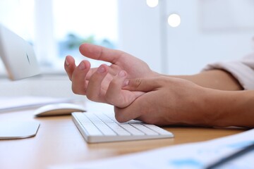 Man suffering from pain in wrist while working on computer at table indoors, closeup. Carpal tunnel...