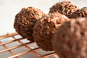 Close-up of chocolate brigadeiros covered in sprinkles on a wire rack.