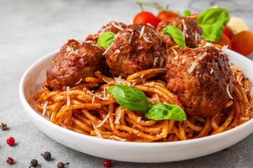 Pasta spaghetti with meatballs in tomato sauce, topped with Parmesan cheese and fresh basil leaves in a plate. Delicious Italian food. Close up