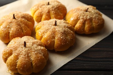 Parchment with tasty pumpkin shaped buns on wooden table, closeup