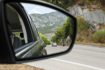The driver looks into the side rearview mirror of the car and sees the road, high mountains and...