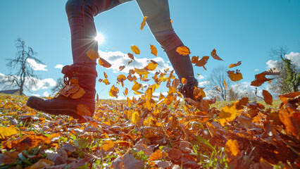 CLOSE UP, LENS FLARE: Female hiker wearing boots runs across a meadow full of beautiful fallen...