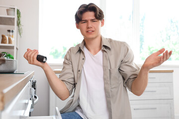 Displeased young man with discharged flashlight in kitchen