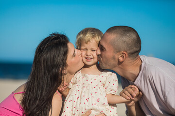 Fototapeta premium Happy family at the ocean. Parents kiss her daughter