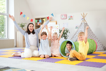 Little children with nursery teacher playing in kindergarten