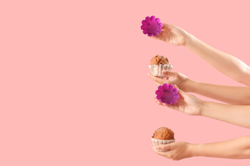 Female hands with baking forms and muffins on pink background