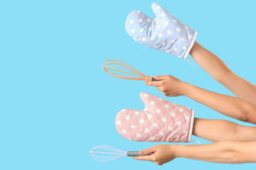 Female hands with whisks and mittens on blue background