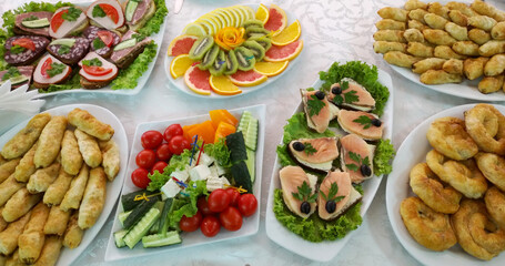 festive banquet table with cold appetizers and pastries. fresh vegetables, sandwiches, fruits and pastries on a table covered with a white tablecloth. holiday or celebration