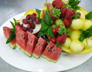 assorted ripe fruits and berries on a white plate. watermelon, melon, peach, grapes and raspberries. decorated with mint sprigs. vitamins, antioxidants and microelements. proper nutrition and diet