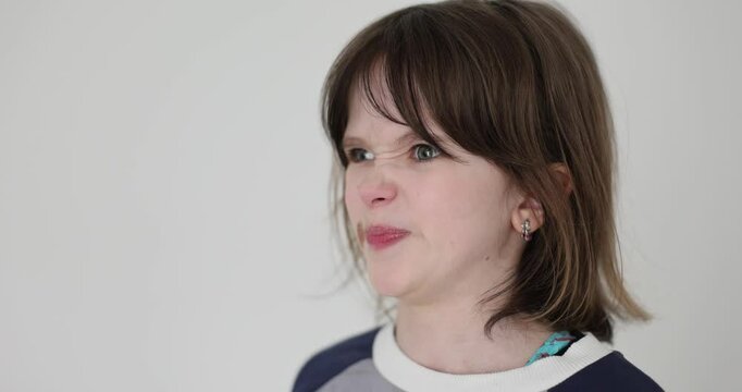 Little girl with brown hair makes funny faces demonstrating emotions on white background. Pretty child expresses disgust confusion and surprise