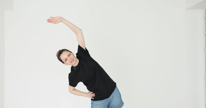 Woman performs lateral flexion stretching exercise on white background. Happy female demonstrates commitment to fitness and active healthy lifestyle