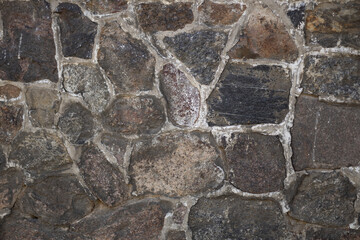 Close-up of a natural stone wall with textured surface on a sunny day. Concept of architecture, construction materials, and rustic outdoor backgrounds