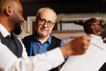 Close up of master tailor teaching skillful craftmanship to aspiring fashion design apprentices in atelier workspace. Diverse team of couturiers working together on bespoken sartorial garments