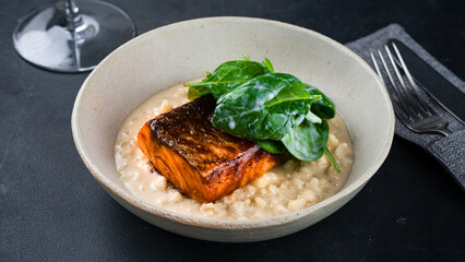 Grilled salmon fillet with creamy risotto and spinach in plate.