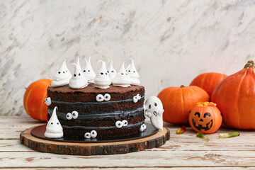 Sweet Halloween cake decorated with meringue ghosts and pumpkins on white wooden table