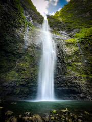 Long exposure scenic view of Hanakapiai Falls, a waterfall at the end of Hanakapiai Valley hiking trail, Kauai, Hawaii, USA against blue sky with clouds