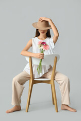 Beautiful young woman with gerbera flowers sitting on chair against grey background