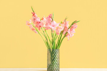 Glass vase with bouquet of beautiful gladiolus flowers on white table against yellow background