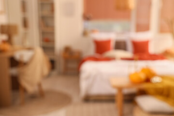 Interior of stylish bedroom with comfortable workplace, coffee table, plaid and pumpkins, blurred view