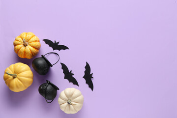 Paper bats with cauldrons and fresh pumpkins for Halloween party on lilac background