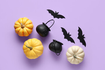Paper bats with cauldrons and fresh pumpkins for Halloween party on lilac background