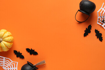 Black bats with paper spider web, cauldrons and fresh pumpkin for Halloween party on orange...