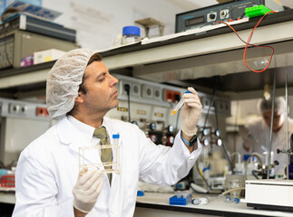 Middle-aged Latin male scientist researcher holding tripod and looking at reaction in test tube...