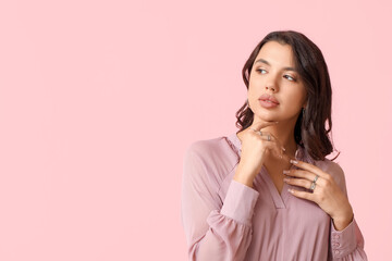 Fashionable young woman in beautiful rings and earrings on pink background