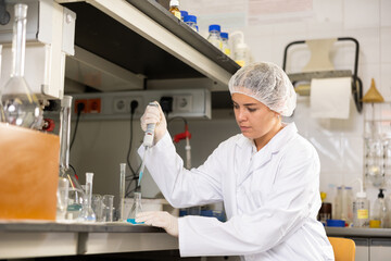 Scientific researching in laboratory. Focused young female pipetting reagent into solution in test...