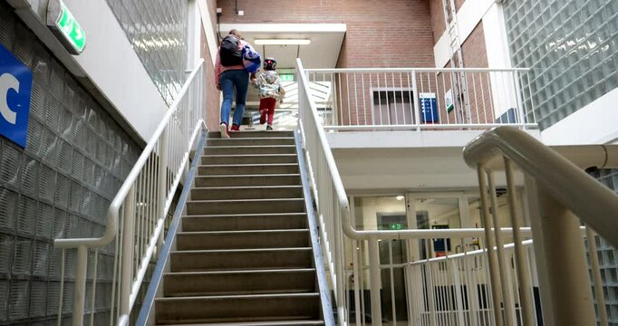A single mother and her son climb a staircase in a building resembling a prison, captured from a low-angle rear view