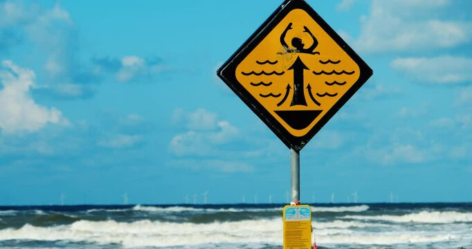 Zoomed-out view of a rip currents warning sign on a Dutch beach with offshore wind turbines, highlighting a dangerous zone for watersports