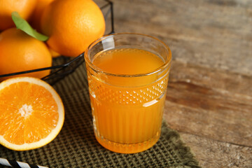 Glass of fresh orange juice and basket with fruits on wooden background