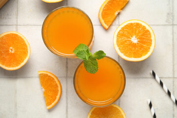 Glasses of fresh orange juice with mint and cut fruits on white tile background