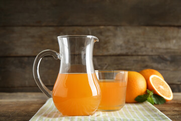 Glass and jug of fresh orange juice with mint on wooden background