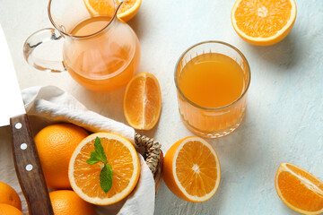 Glass and jug of fresh orange juice with mint on light blue background