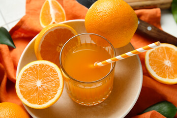 Glass of fresh orange juice and plate with fruits on white tile background