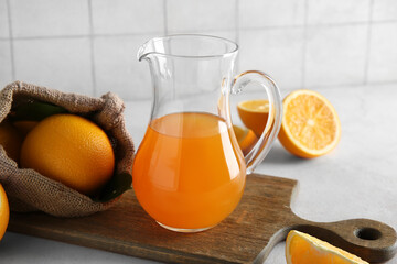 Jug of fresh orange juice and sack bag with fruits on white table