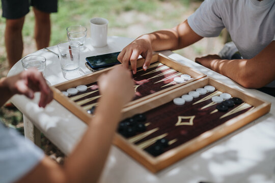 A group of friends playing backgammon on a sunny day, creating a relaxed and fun atmosphere. Ideal for portraying leisure activities and friendship.