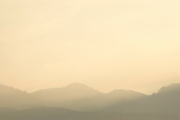 A serene landscape unfolds at dusk. Rolling hills fade into a hazy horizon, bathed in soft, golden...