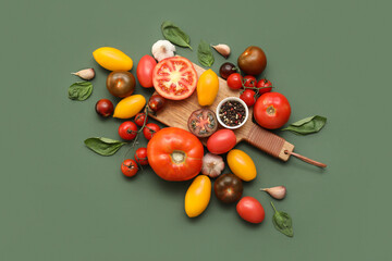 Wooden board with different fresh tomatoes, garlic, basil and bowl of peppercorn on green background