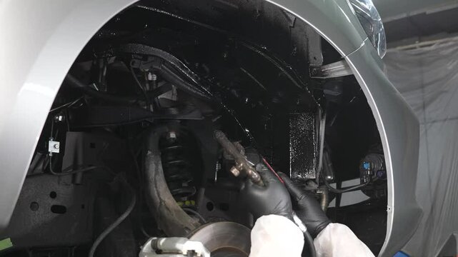 The master sprays an anti-corrosion compound on the bottom of the car. 