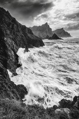 Dramatic black and white seascape with crashing waves against rugged cliffs, capturing the raw beauty of nature.