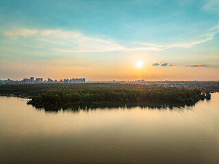 Big lake with green shores in bright sun light and city on horizon, aerial landscape. Recreation concept. Aerial view