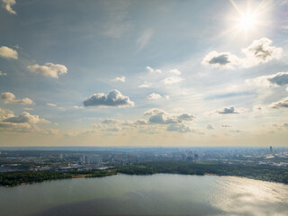 Big lake with green shores in bright sun light and city on horizon, aerial landscape. Recreation concept. Aerial view