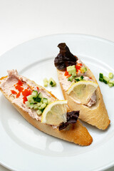 Tasty open-faced sandwiches with tuna spread, topped with fresh vegetables and lemon slices on a white plate