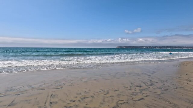 panning footage along Coronado Beach with blue ocean water, white sand, lush green palm trees, people, blue sky and clouds in Coronado California USA