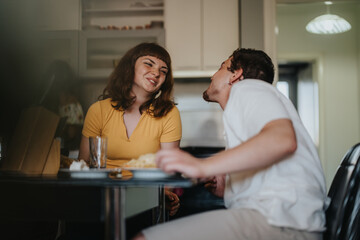 A young couple shares a joyful moment while having a meal in their kitchen. The scene captures...