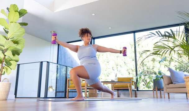 Exercising with dumbbells, plus size woman doing yoga in modern living room, at home